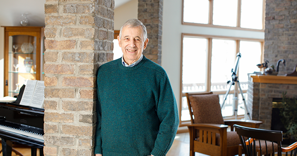 Alan Kosak standing against a brick column with a green sweater on