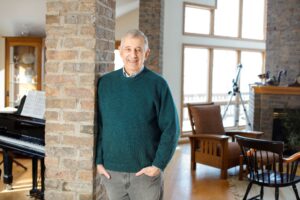 Alan Kosak standing against a brick column with a green sweater on