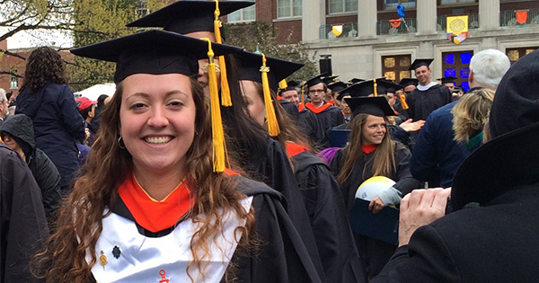 Mary Bucklin ’16 in cap and gown, in front of Rush Rhees library.