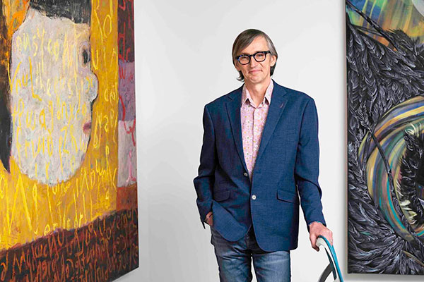 Stephen Dewhurst smiles with paintings to his left and right