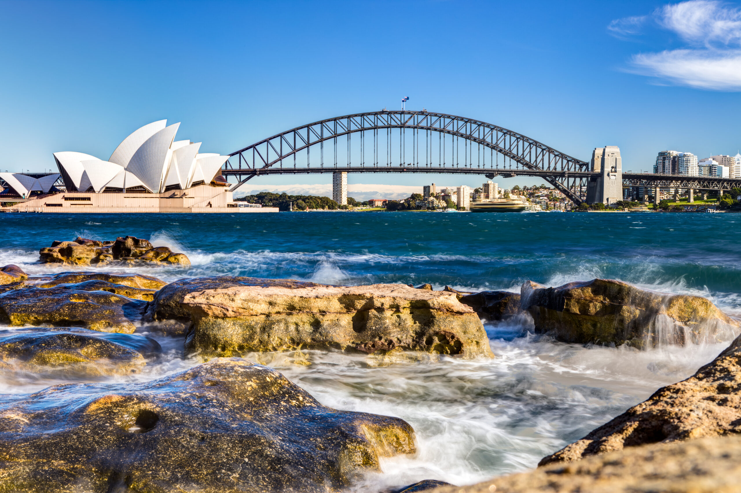 Sydney Opera house, with the bridge, and water and rocks in the foreground