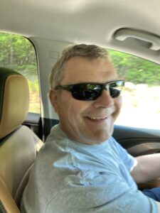 LeFrois sitting in a car smiling for the camera with sunglasses on