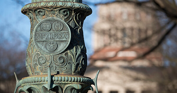 meliora seal at base of flagpole with rush rhees in background
