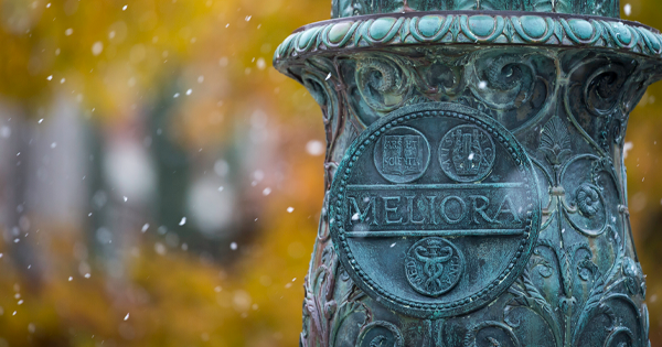 Eastman Quad stone monument with Meliora written, along with three symbols while snowing and fall leaves in background