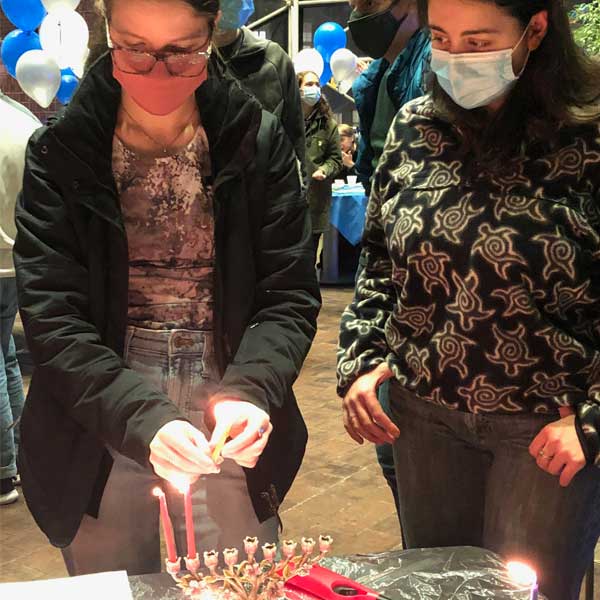 two students lighting the third candle on a menorah