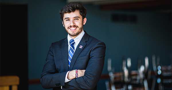 Anis Kallel ’17 (KEY) hands crossed in a blue suit and blue tie