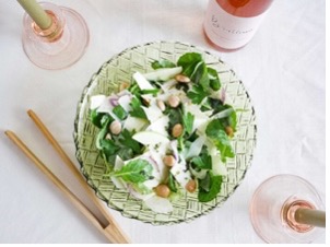 a salad bowl placed on the center of a table with a bevaergae to the side along with utensils