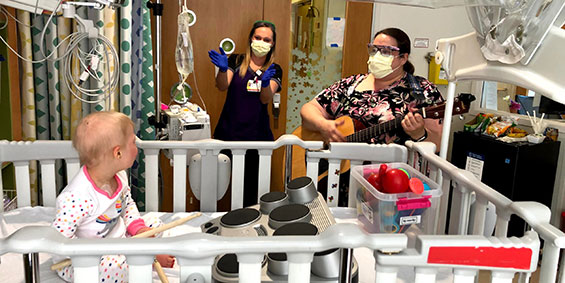 two staff playing musical instruments with a child whom is in a crib. 
