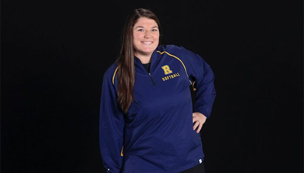 Abby Hurley-Martin posing in front of black background wearing blue Rochester R shirt
