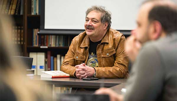 Dmitry Bykov wearing a brown leather jacket speaking while seated at a table