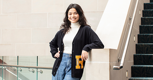 Ashni Budge, in a Blue UR cardigan standing next to a staircase