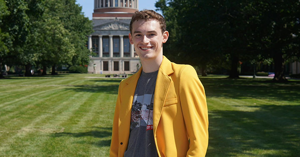 Ethan King in a yellow blazer in the quad in front of Rush Rhees library