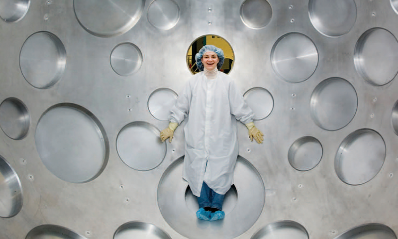 Woman in white lab coat lying again't a steel cover surface full of circles