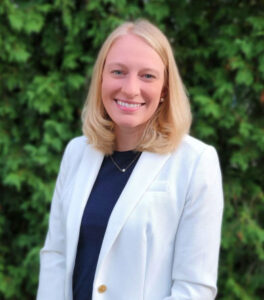 Abby Zabrodsky ’14, ’19S (MBA) standing in front of green leaf wall in white jacket