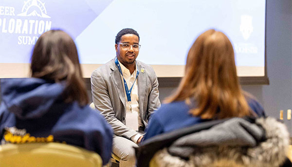 Jamal Holtz sits and speaks to students seen from behind.