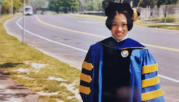 Joanne Y. Law dressed in cap and gown on the site of the road