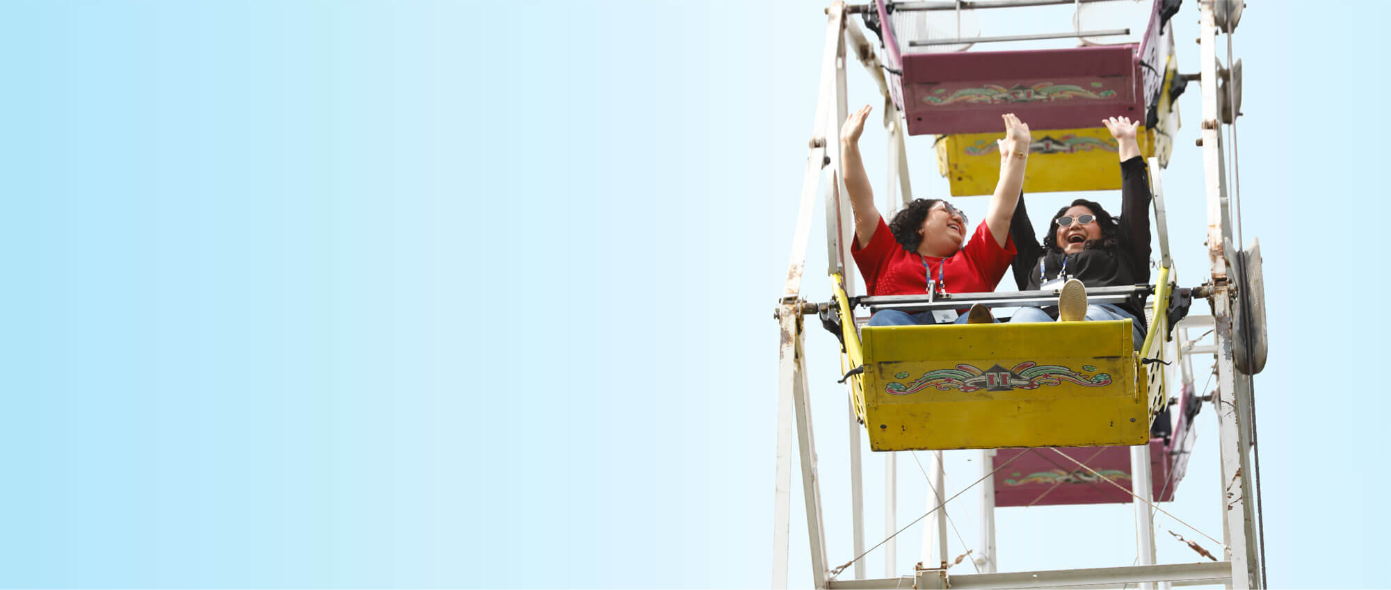 Two women on ferris wheel holding arms in the air