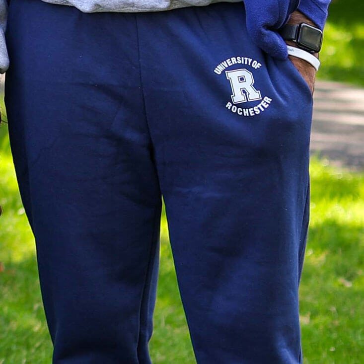 A close-up of navy University of Rochester sweatpants with the school’s logo printed on the thigh.