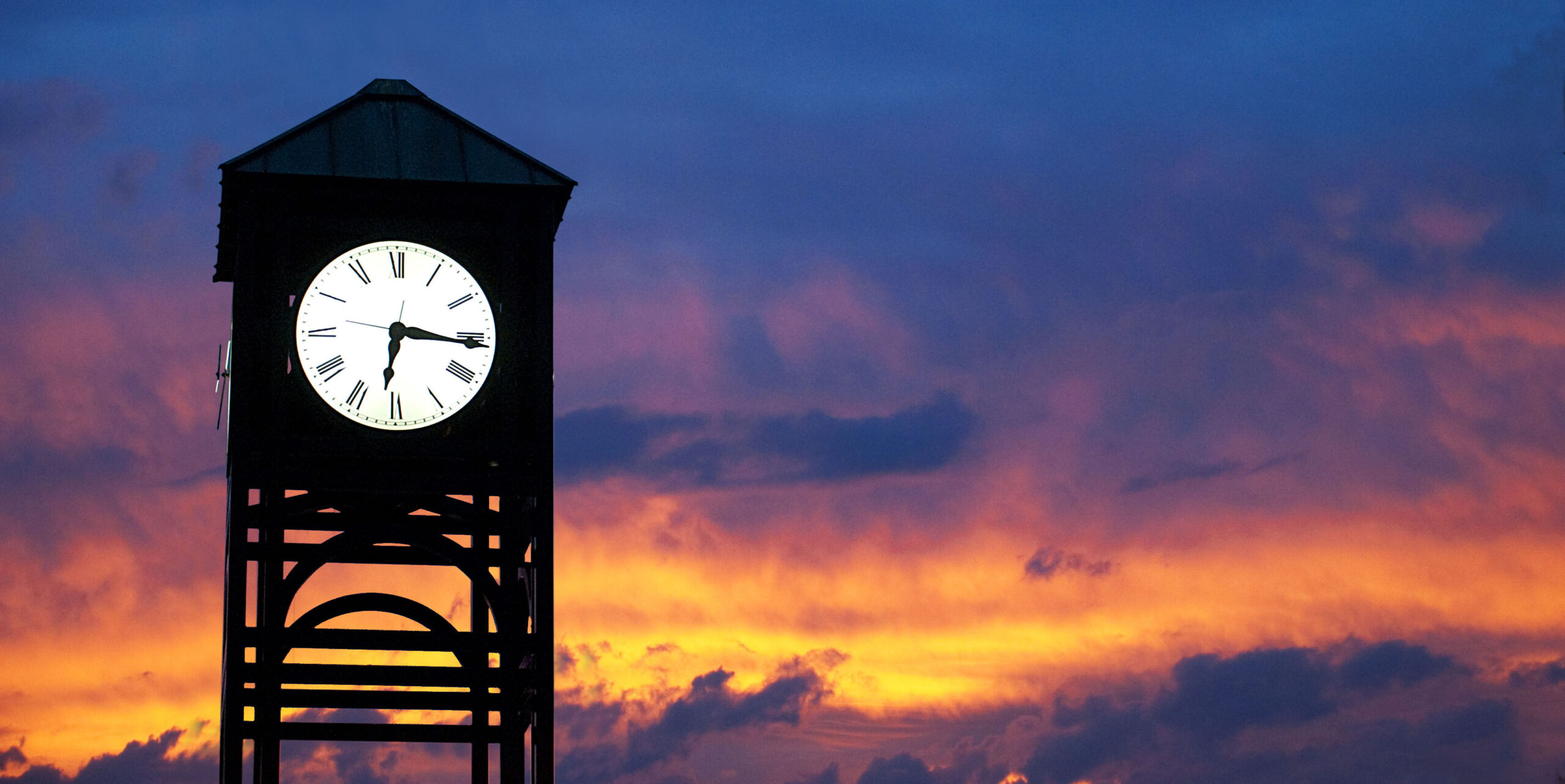 A clock tower against a sky with purple clouds and golden sunlight peaking through