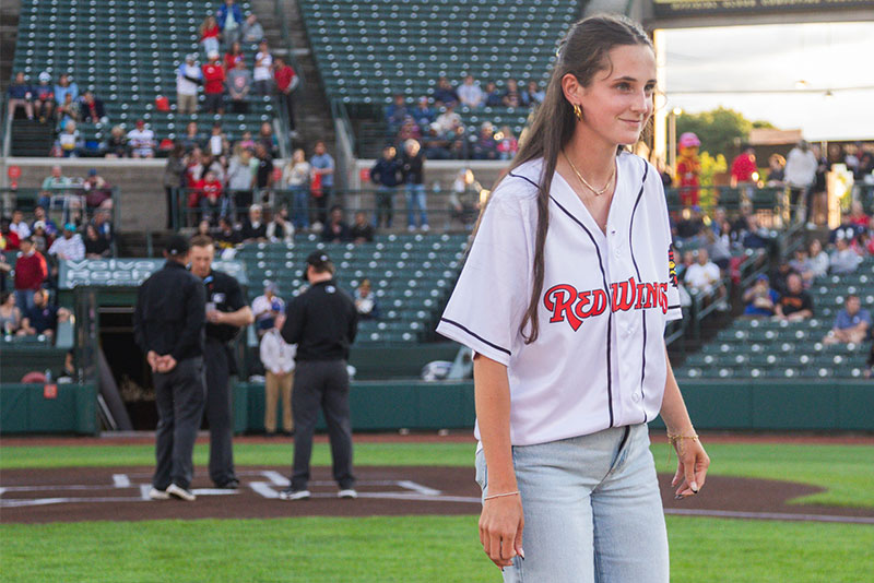 Maddie-Anania-Red-Wings Maddie Anania wearing a Red Wings Jersey out on the baseball field stadium