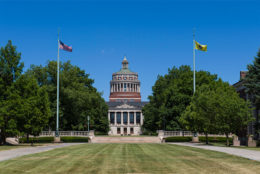 Rush Rhees Library with blue sky and two flag poles