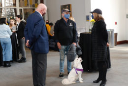 three people in conversation wearing masks and a white dog is at their feet