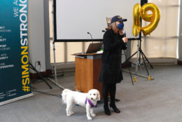 woman in cap, mask and mic in hand next to white dog