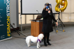 woman in cap, mask and mic in hand next to white dog