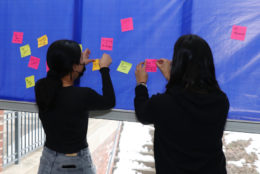 two women placing colorful sticky notes on blue board