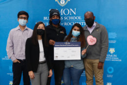 five people wearing masks holding a i heart simon business school because sign