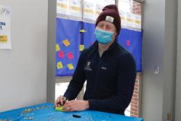 man filling out sticky note at a table posing for photo wearing a mask and knit hat