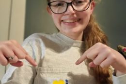 female student in glasses smiling and pointing to i hear warner on her tshirt