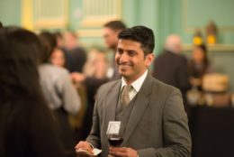 man in suit holding a glass of wine smiling at an event