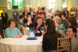 man holding up a glass for a toast seated at table with other event attendees