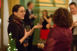 women wearing glasses with glass of wine in hand speaking to another woman