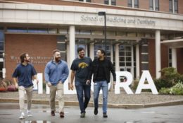 four men walking away from SMD building with meliora letters behind them