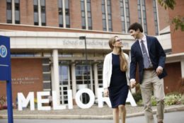 couple holding hands walking in front of SMD meliora letters