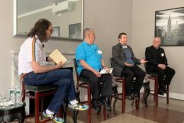 four men on high top chairs giving talk in front of audience