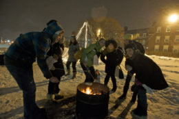 group of people outdoors roasting marshmellows on a winter day