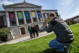 man squatting taking photo of three people in front of rush rhees library