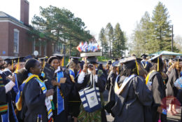 graduate pointing camera at photographer in crowd of other students