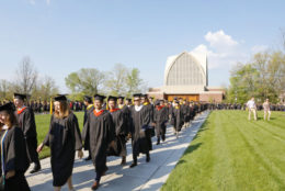 graduates walking into commencement with building and blue skies in background