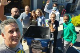 group of volunteers smiling for camera in front of a garbage bin
