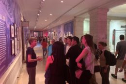 woman in front of group giving talk in front of art exhibit