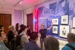 woman in front of group giving talk in front of art exhibit