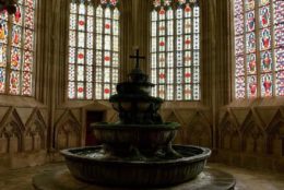 indoors at a old fountain and stained glass windows behind it