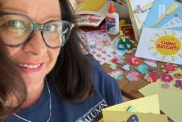 woman in glasses and blue UR alumni tshirt smiling at camera holding a homemade greeting card