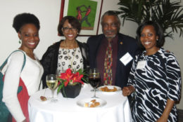 three women and one man posing for photo in front of table with food and drink