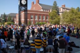 large crowd outdoors in quad with click tower nad brick buildings in background