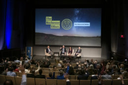 four people on stage with large screen behind them and audience in front